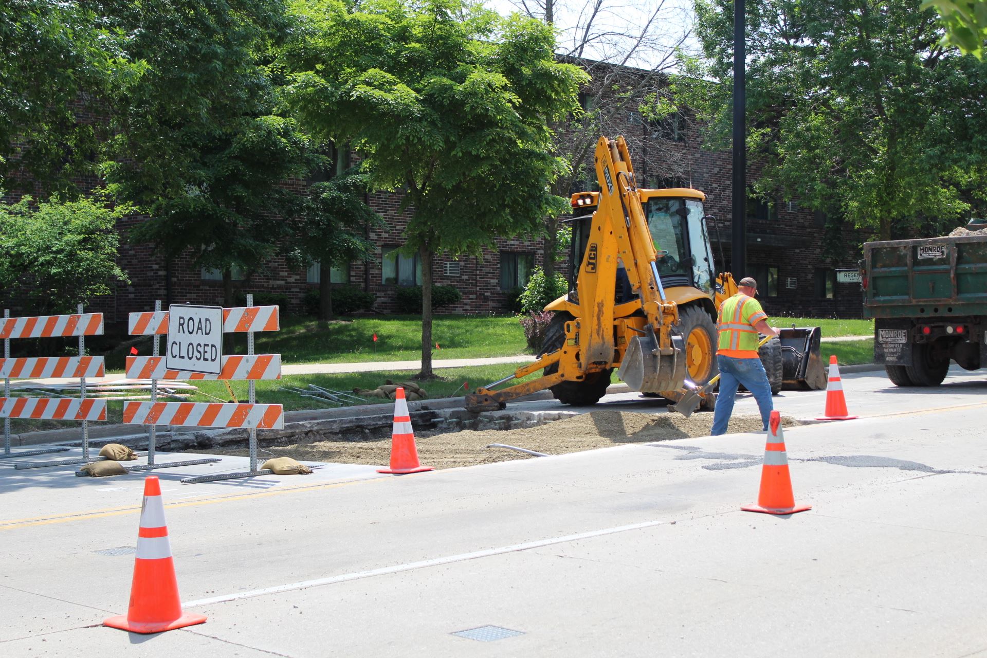 A man shoveling gravel in a hole in a road.