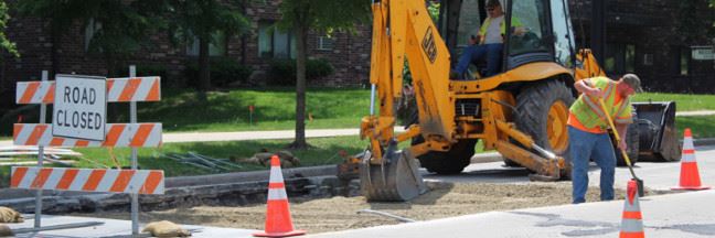 Two men working to fill a large gap in the road.